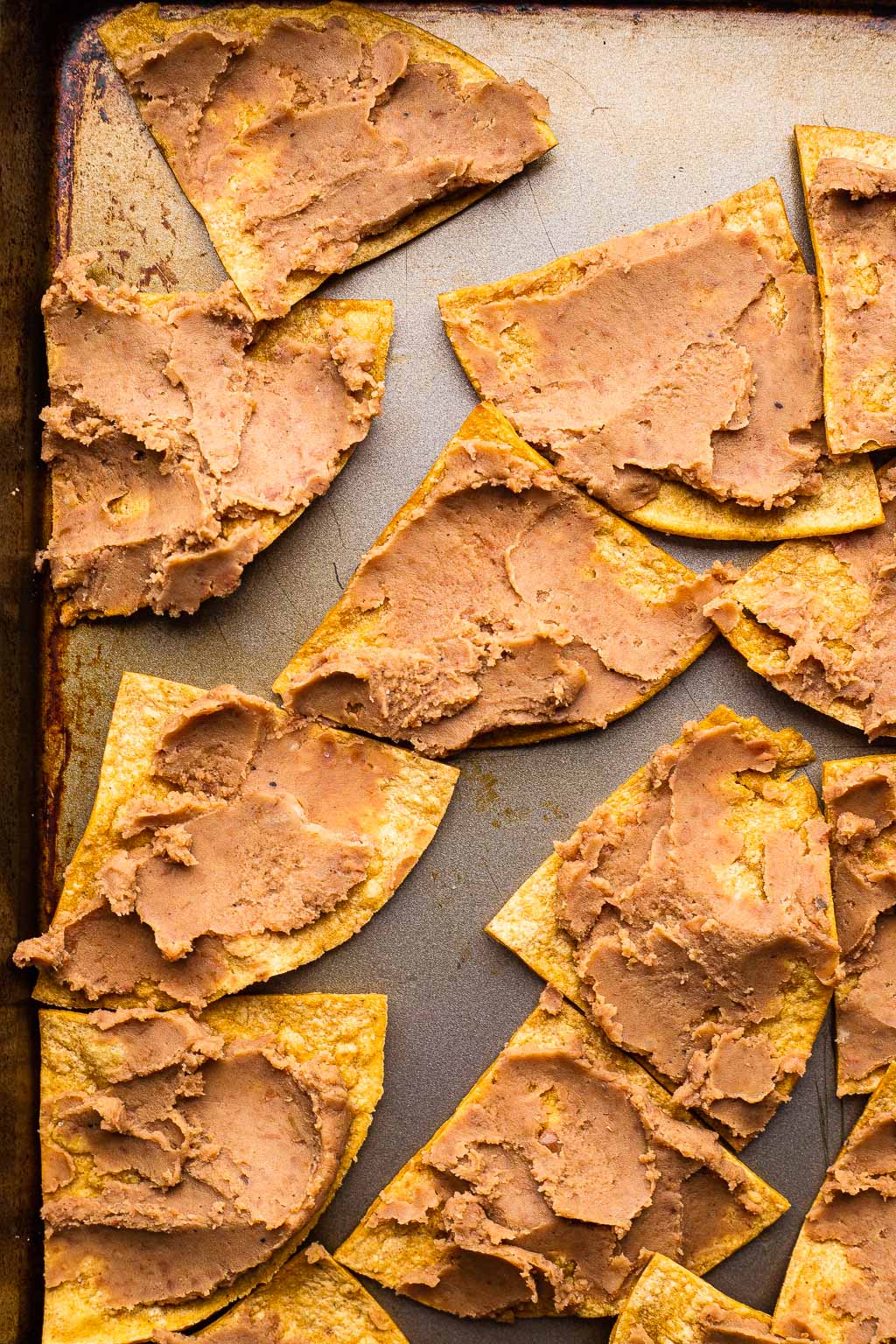 Tortilla chips topped with refried beans on a baking sheet 