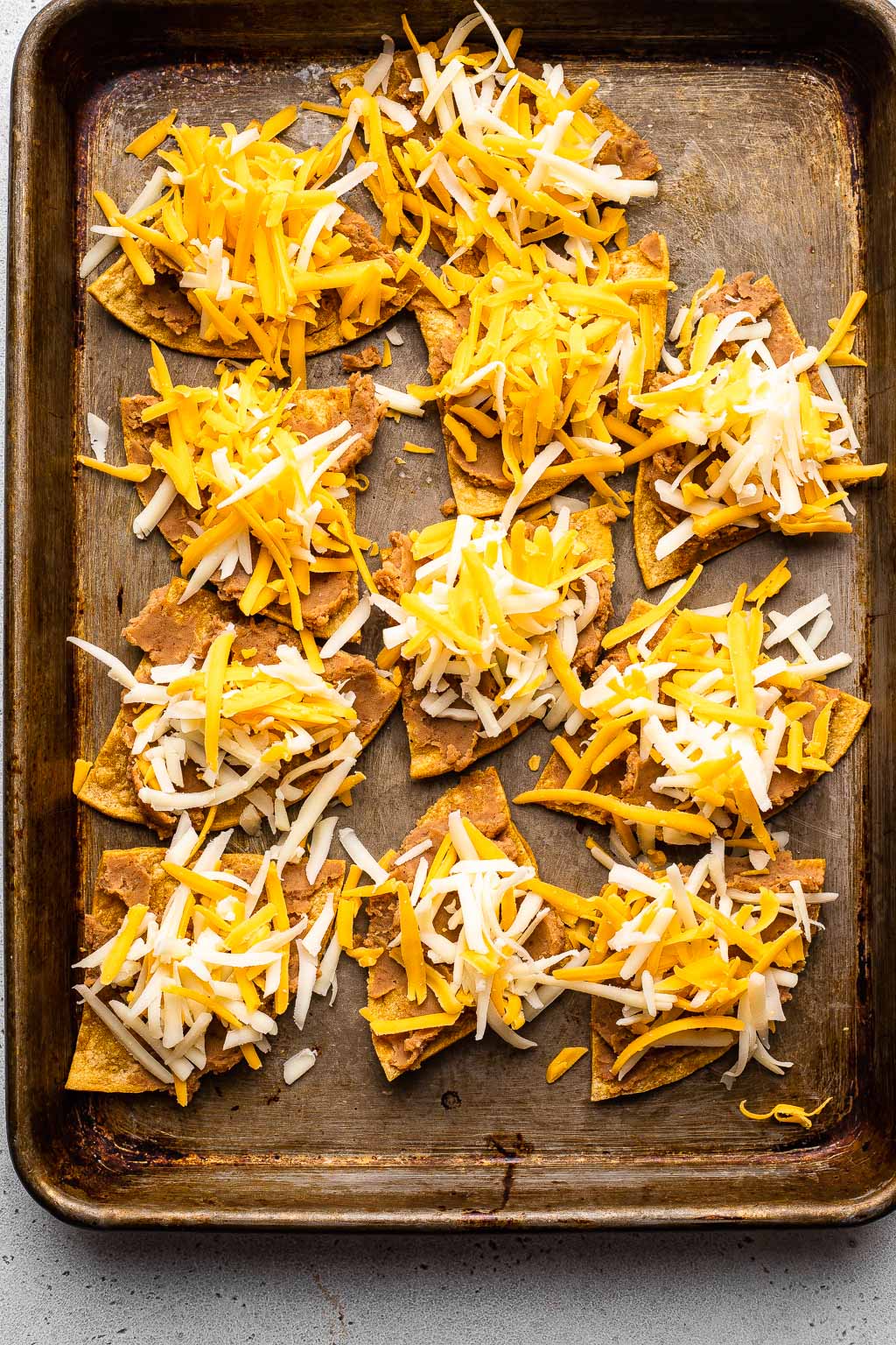 Tortilla chips topped with refried beans and cheese on a baking sheet 