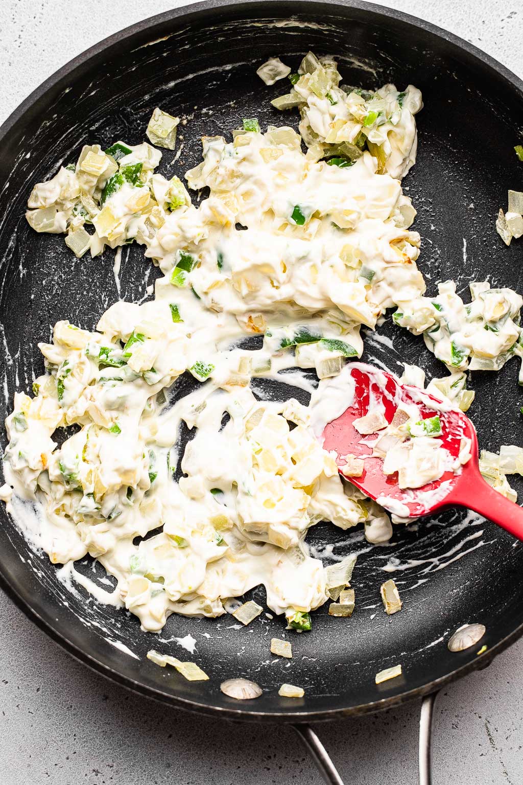Cream cheese being melted in a skillet with onion and jalapeño