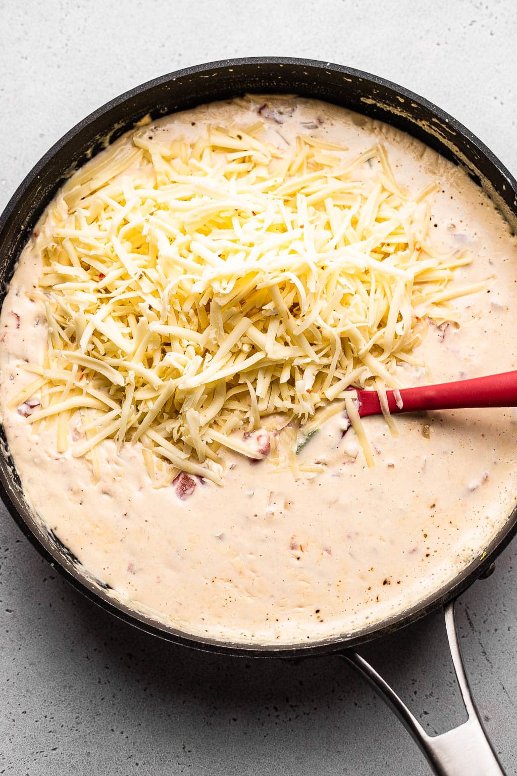 Shredded cheese added to a skillet of queso 
