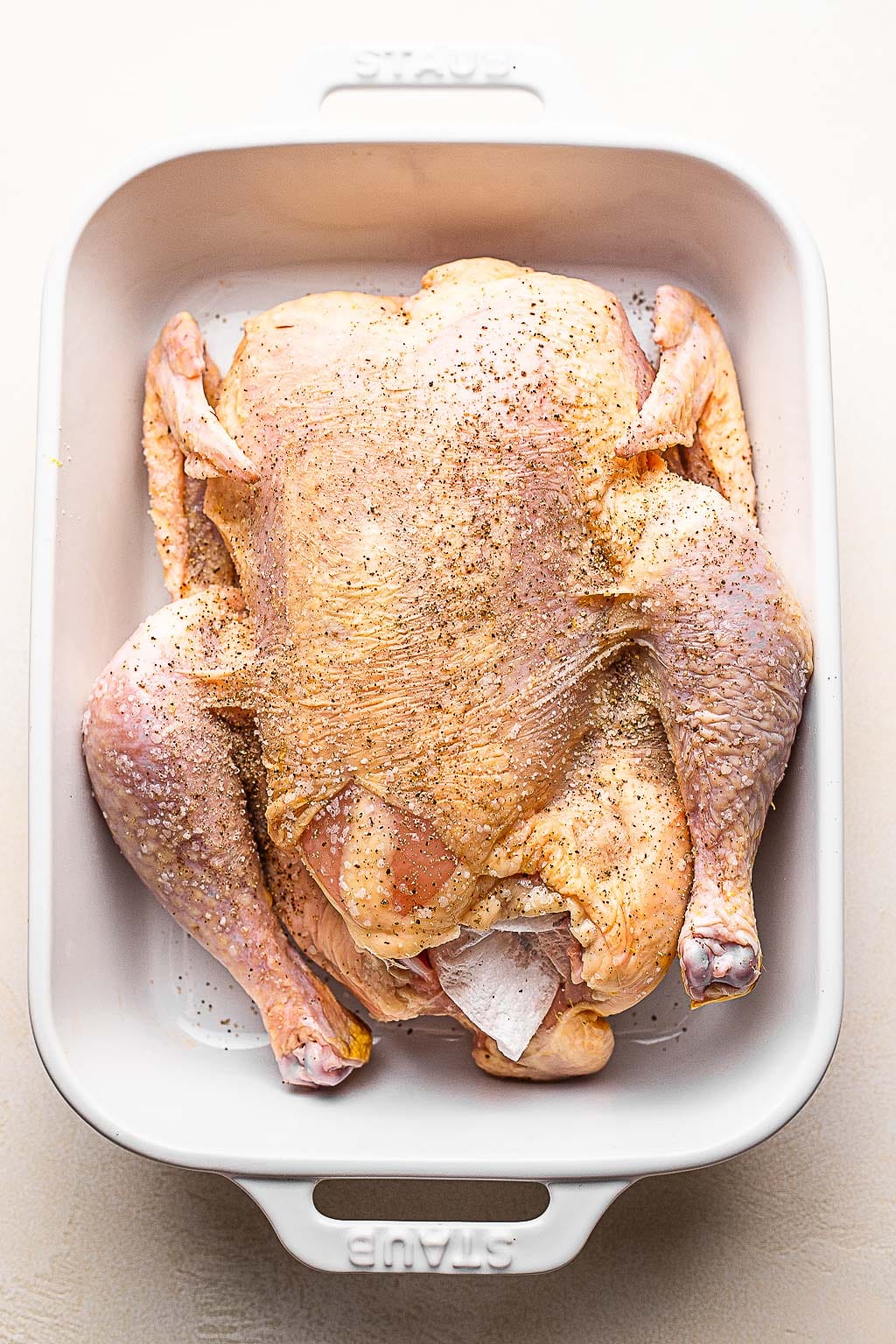 A raw chicken seasoned with salt and pepper 