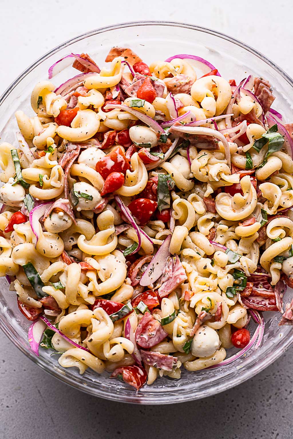 Assembling a grinder-style pasta salad with salami and mozzarella 