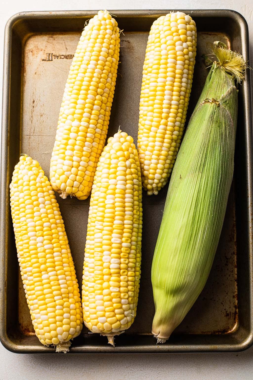 Fresh ears of corn on baking tray 