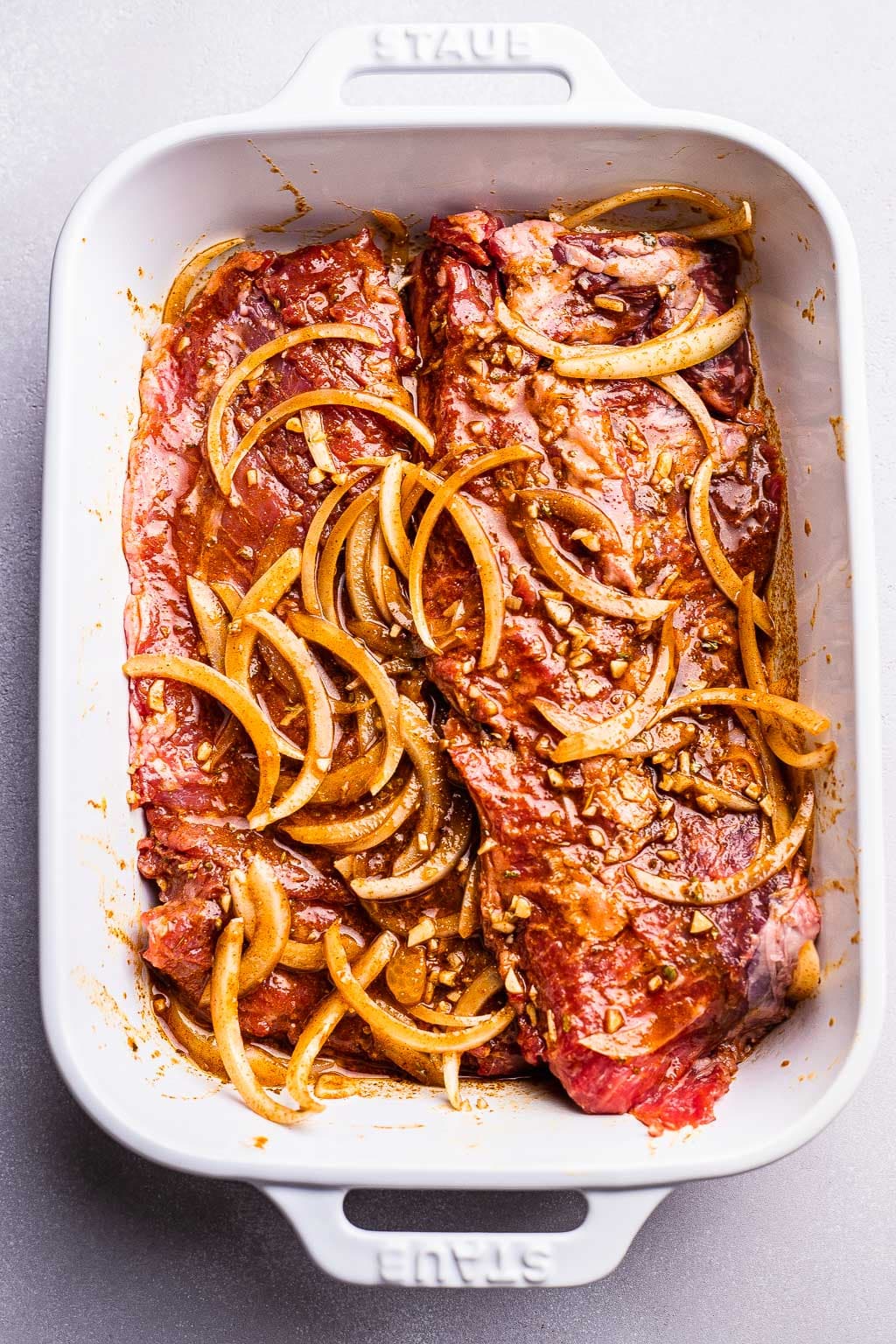 Steak marinating with onions in baking dish 