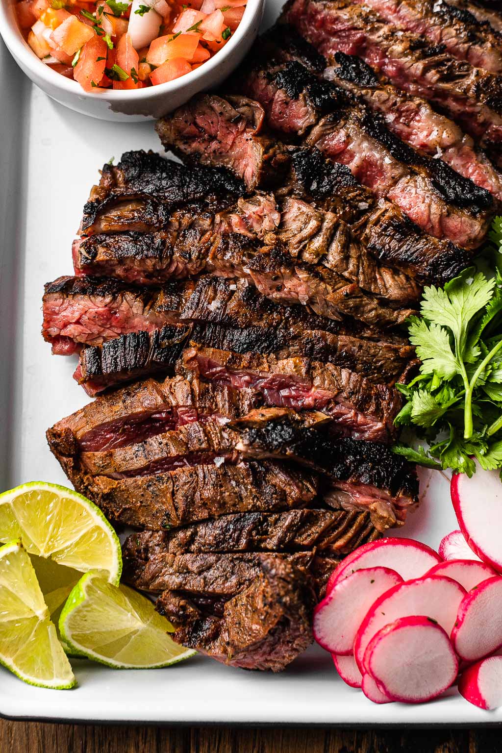 Sliced carne asada on baking tray with radish, cilantro, lime, and pico de gallo. 