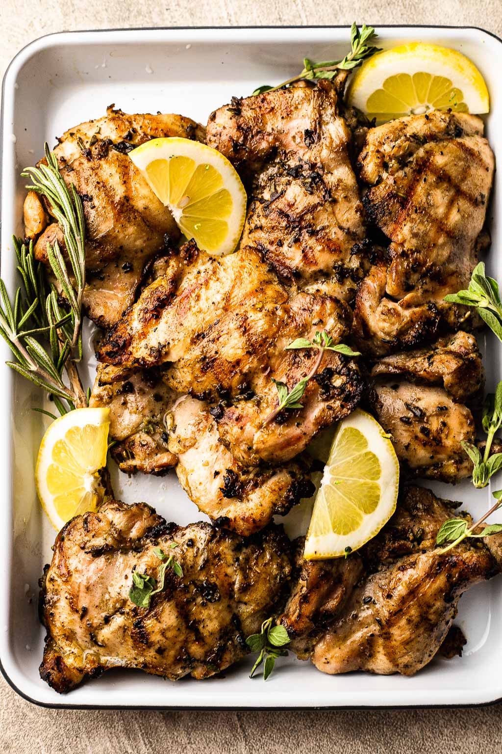 An overhead view of grilled lemon herb chicken on a baking tray. 