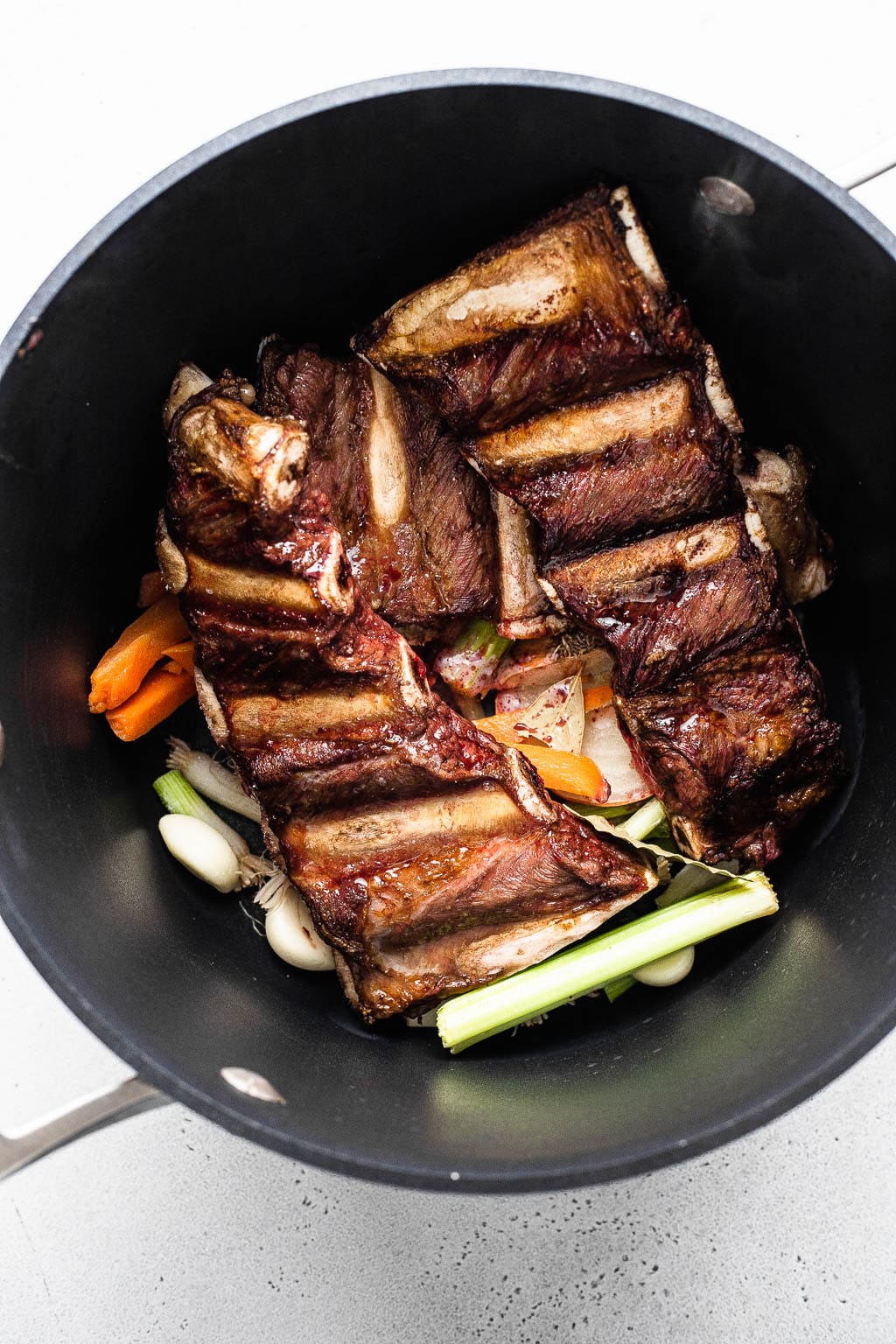 Roasted beef finger ribs and aromatics in a stock pot 