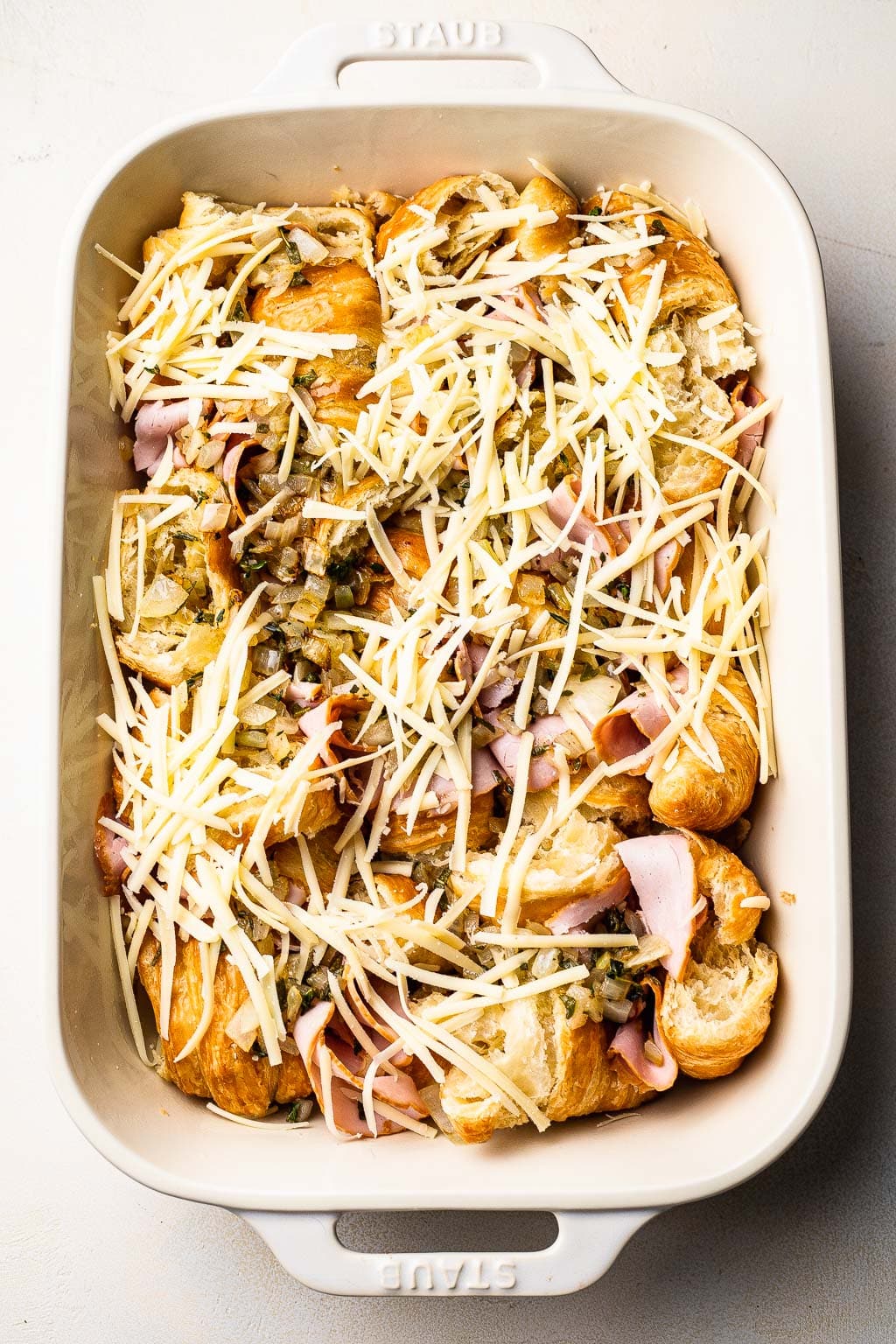 Croissants, ham, and Gruyere cheese layered in a baking dish 