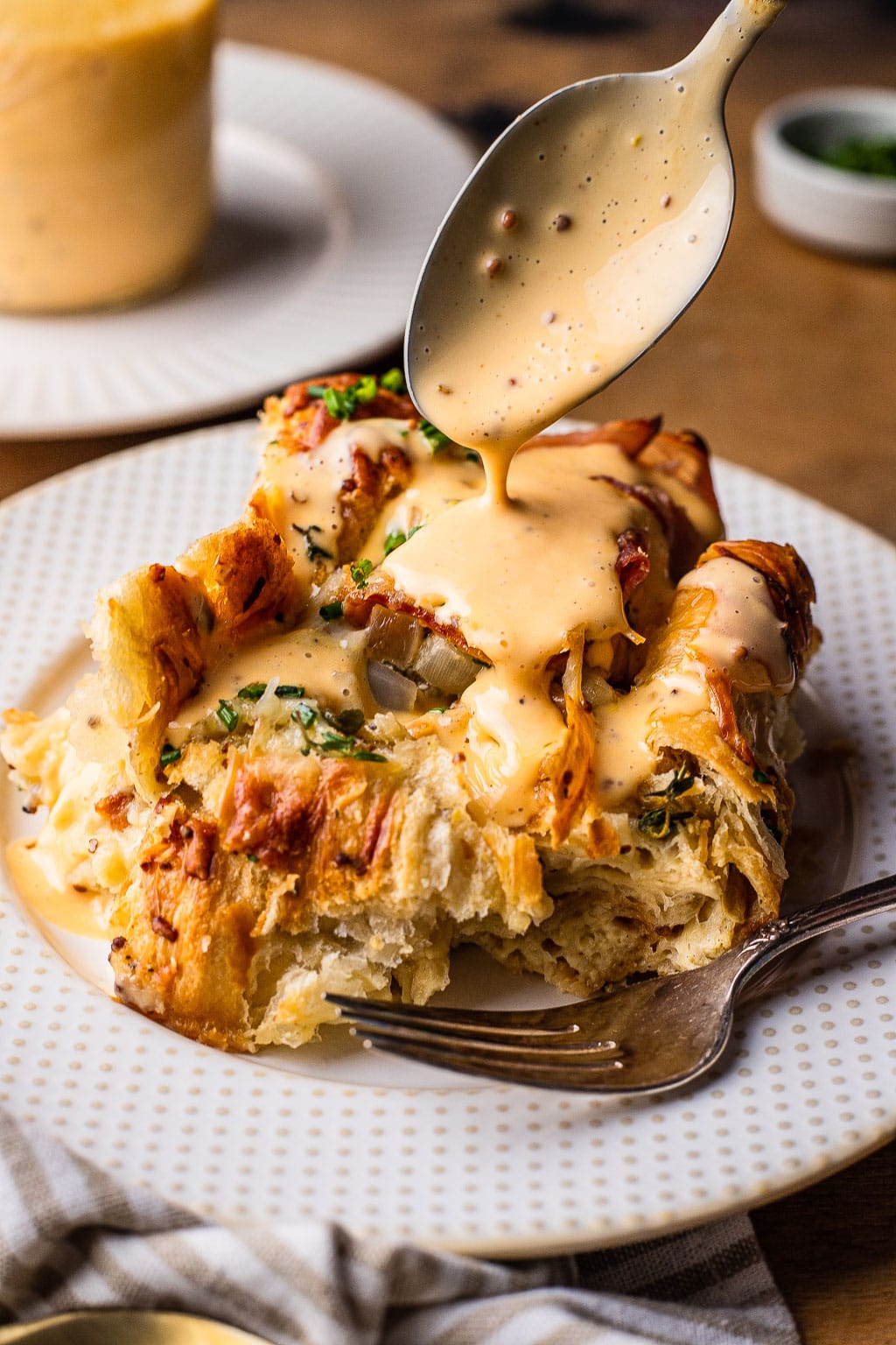 A slice of croissant ham and cheese bake being drizzled with hollandaise sauce 