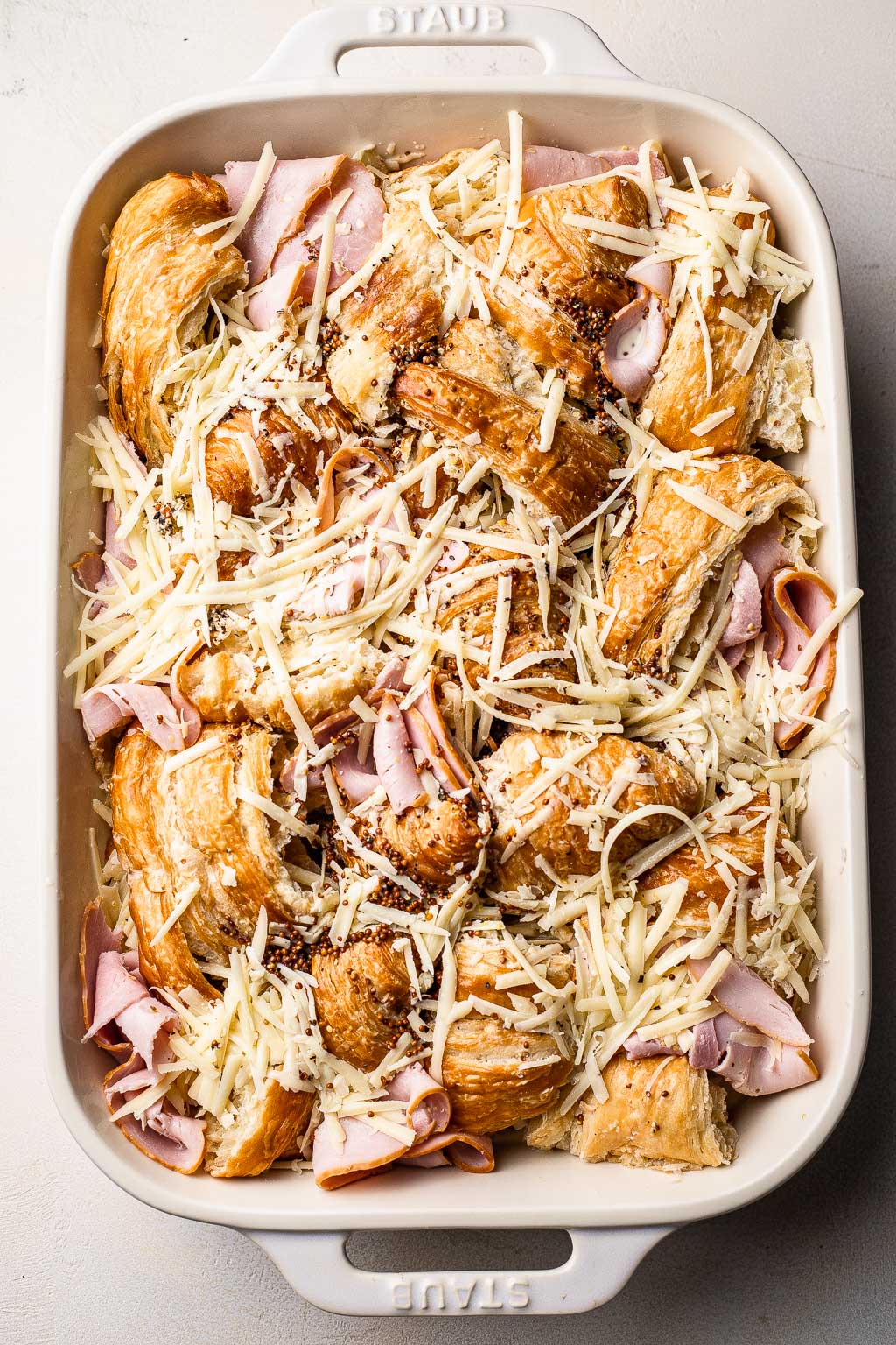 Croissants, ham, and Gruyere cheese layered in a baking dish 
