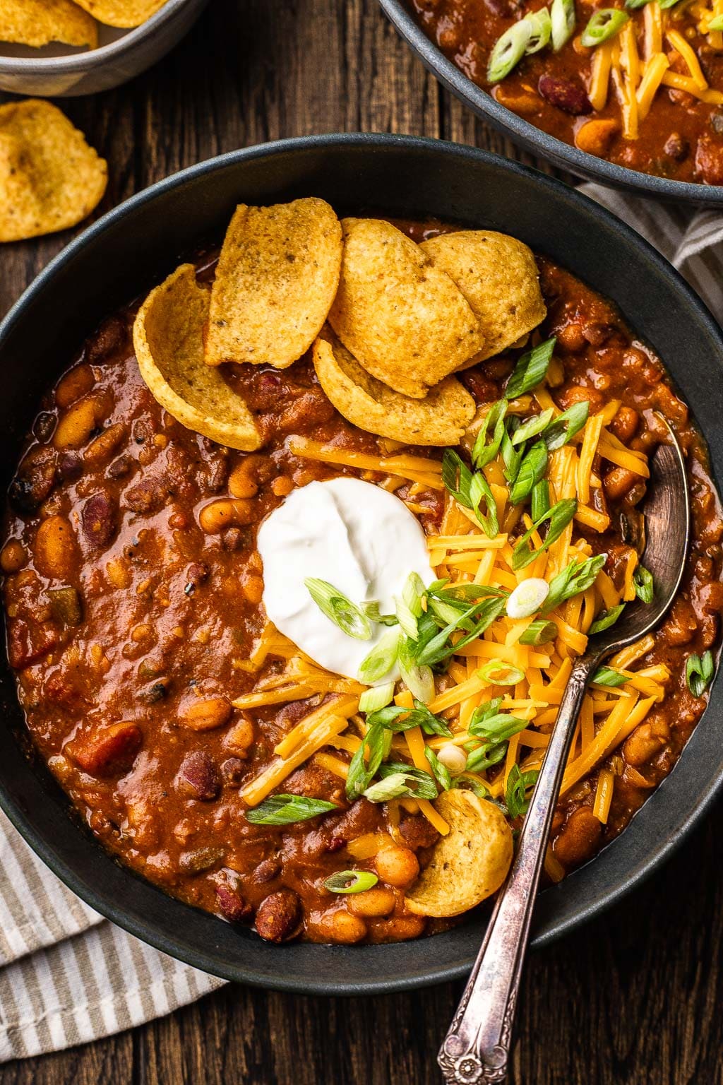 A bowl of 5 bean chili topped with sour cream, shredded cheese, and corn chips. 