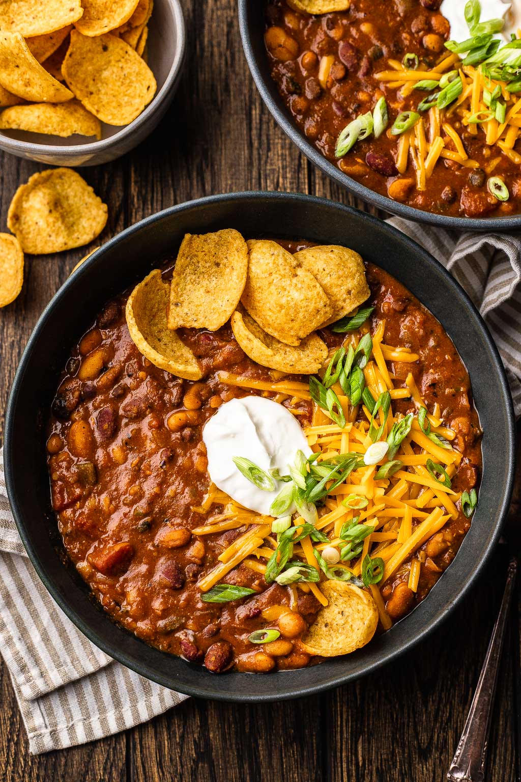 A bowl of 5 bean chili topped with sour cream, shredded cheese, and corn chips. 