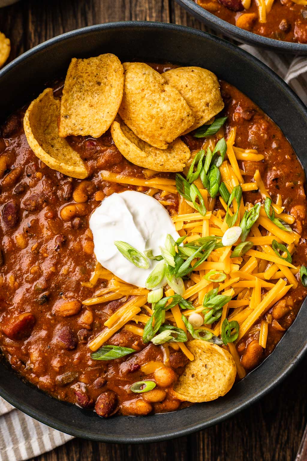 A bowl of vegetarian bean chili topped with sour cream, shredded cheese, and corn chips. 