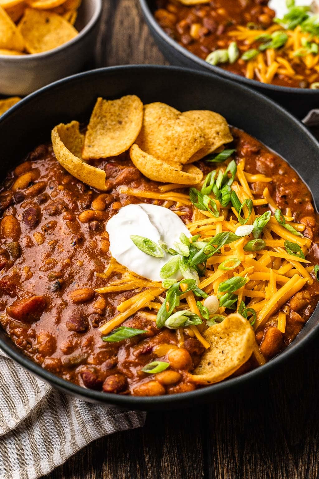 A bowl of 5 bean chili topped with sour cream, shredded cheese, and corn chips. 
