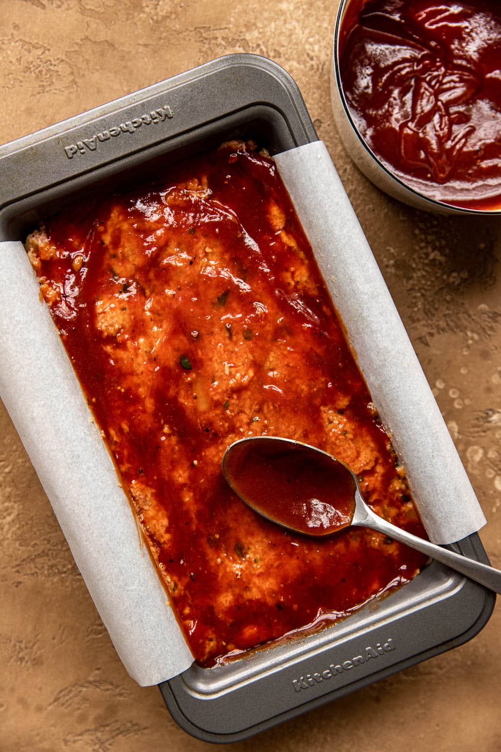 Unbaked turkey meatloaf being spread with ketchup glaze 
