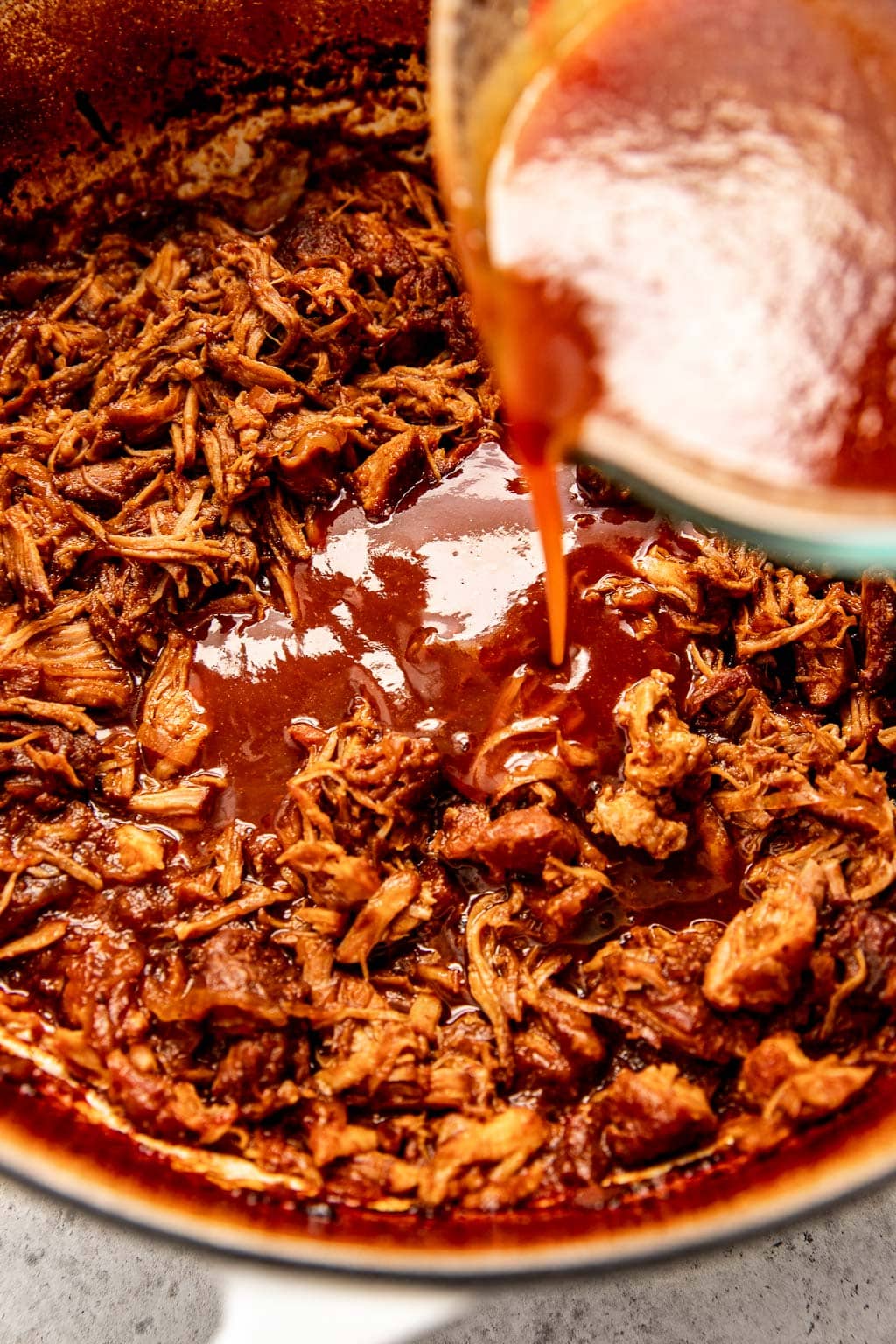 Bbq sauce being poured over pulled pork in dutch oven
