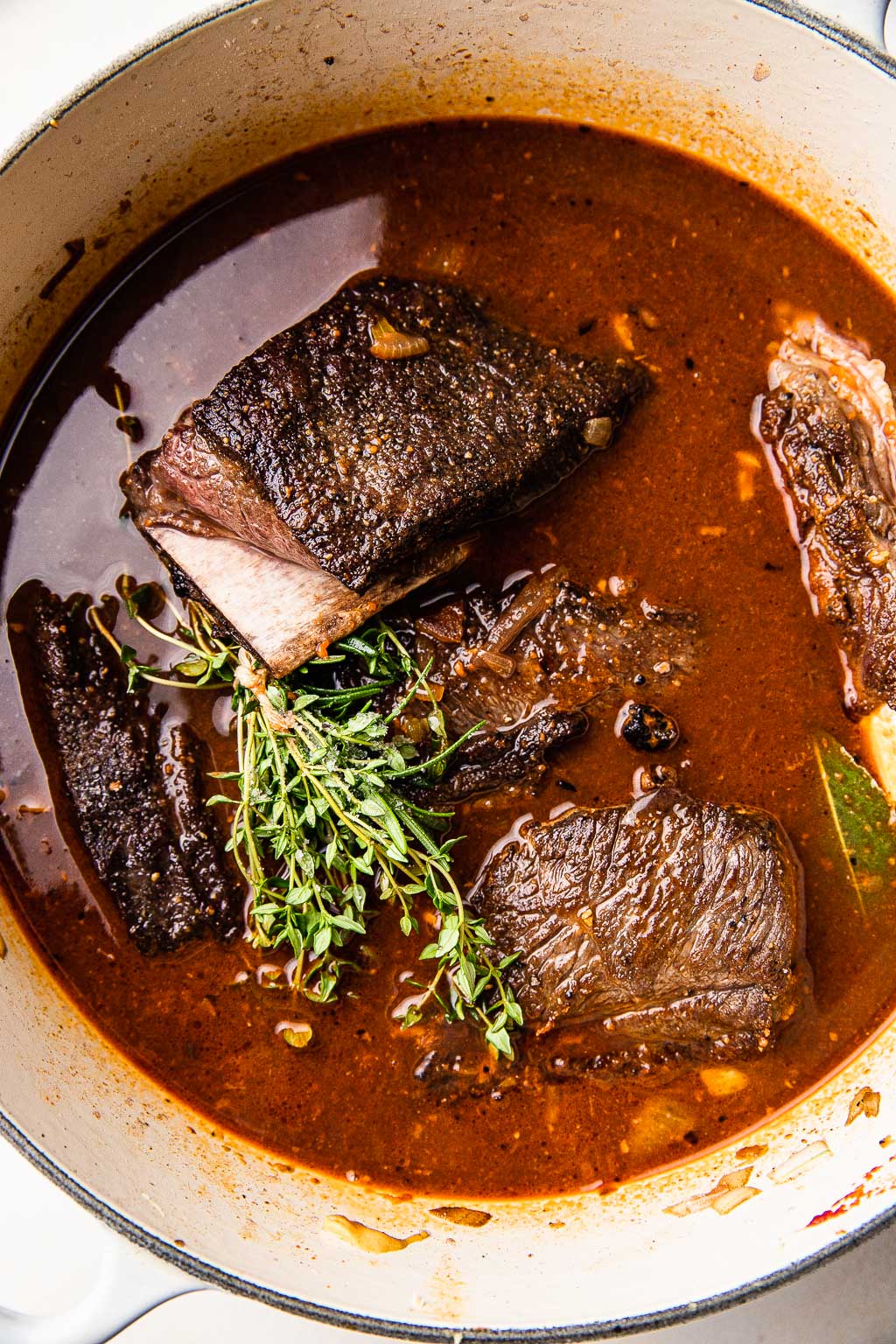 Red wine braised short ribs in a Dutch oven with fresh thyme. 