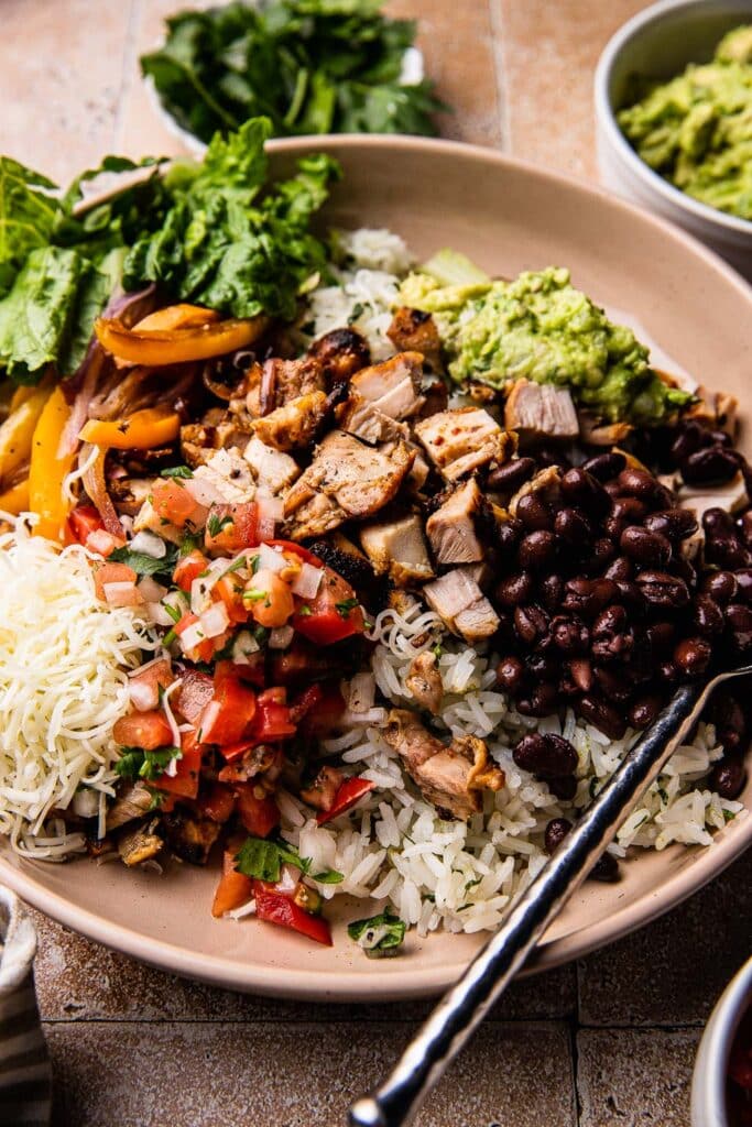 A chipotle chicken burrito bowl topped with beans, guac, pico, and cheese. 