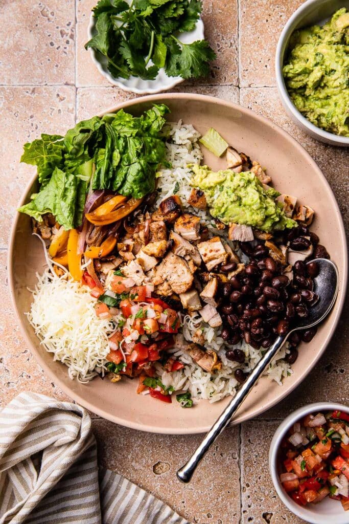 A chipotle chicken burrito bowl topped with beans, guac, pico, and cheese. 