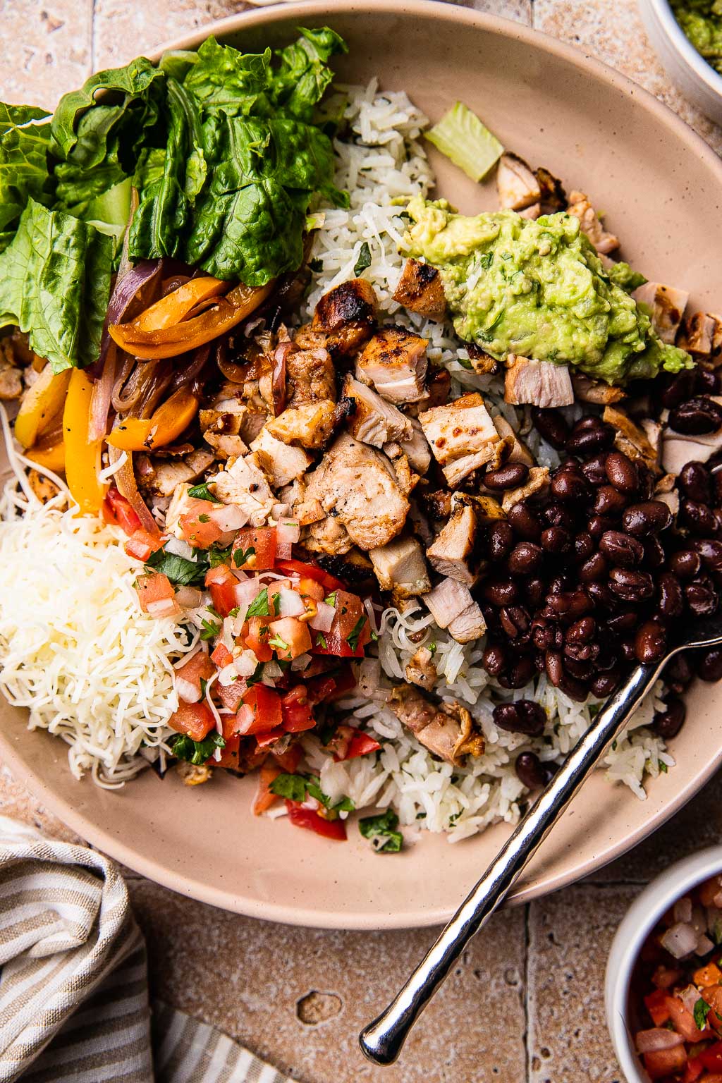 A chipotle chicken burrito bowl topped with beans, guac, pico, and cheese. 