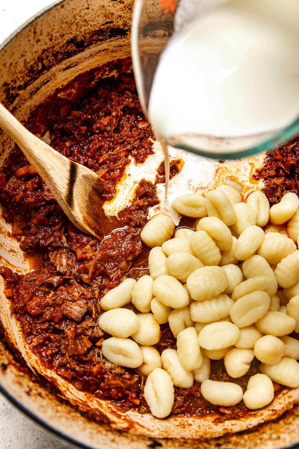 Gnocchi and heavy cream being added to a pot of ragu sauce
