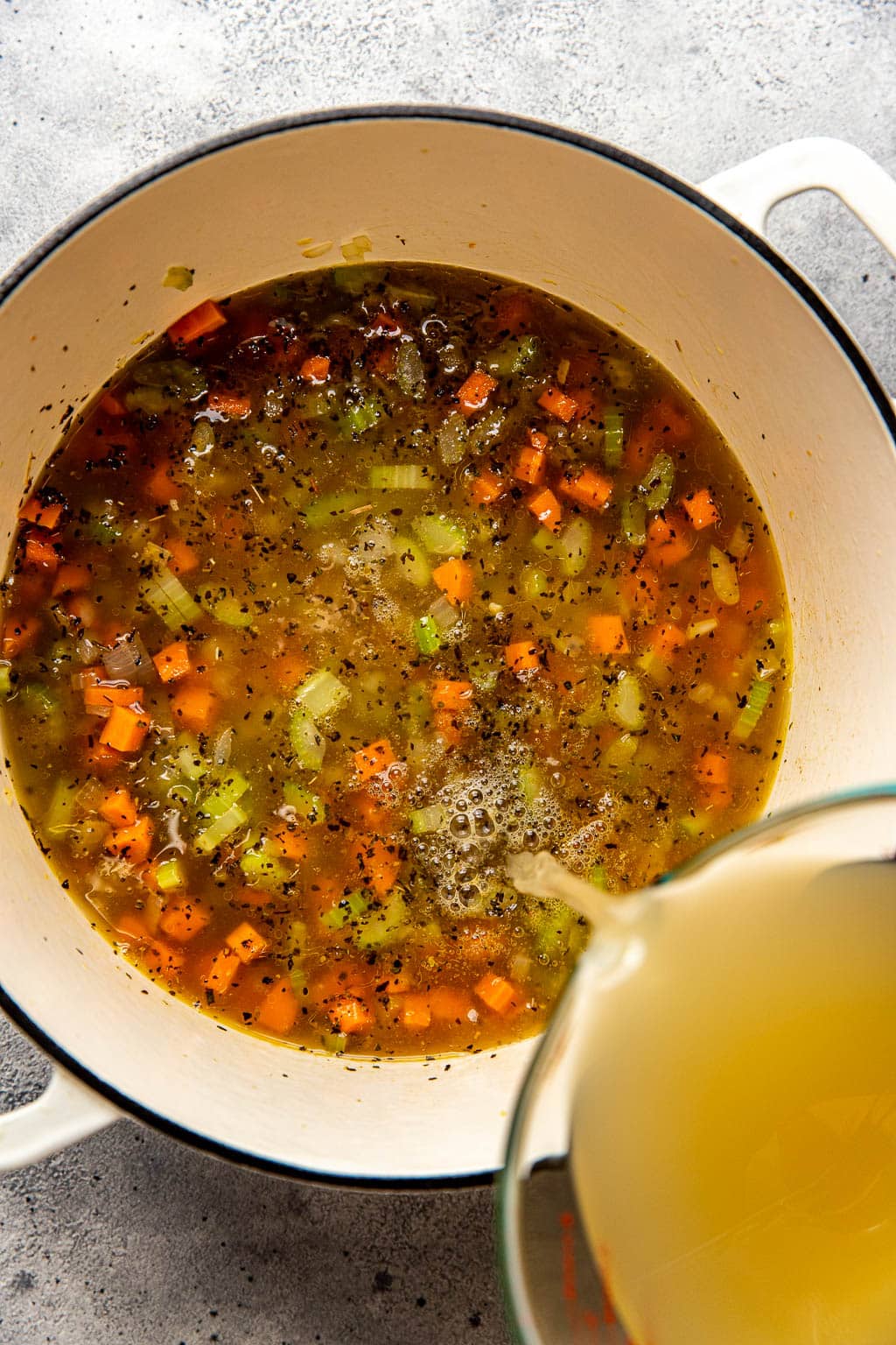 Chicken stock being poured into a pot of soup 
