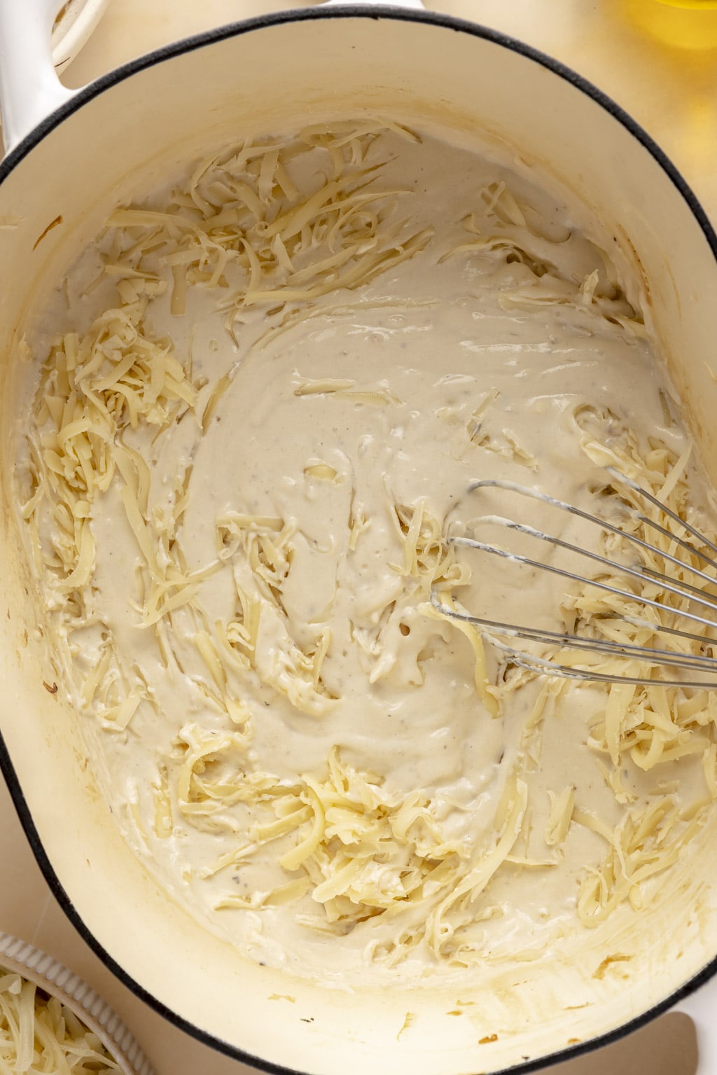 Shredded cheese being stirred into béchamel sauce. 