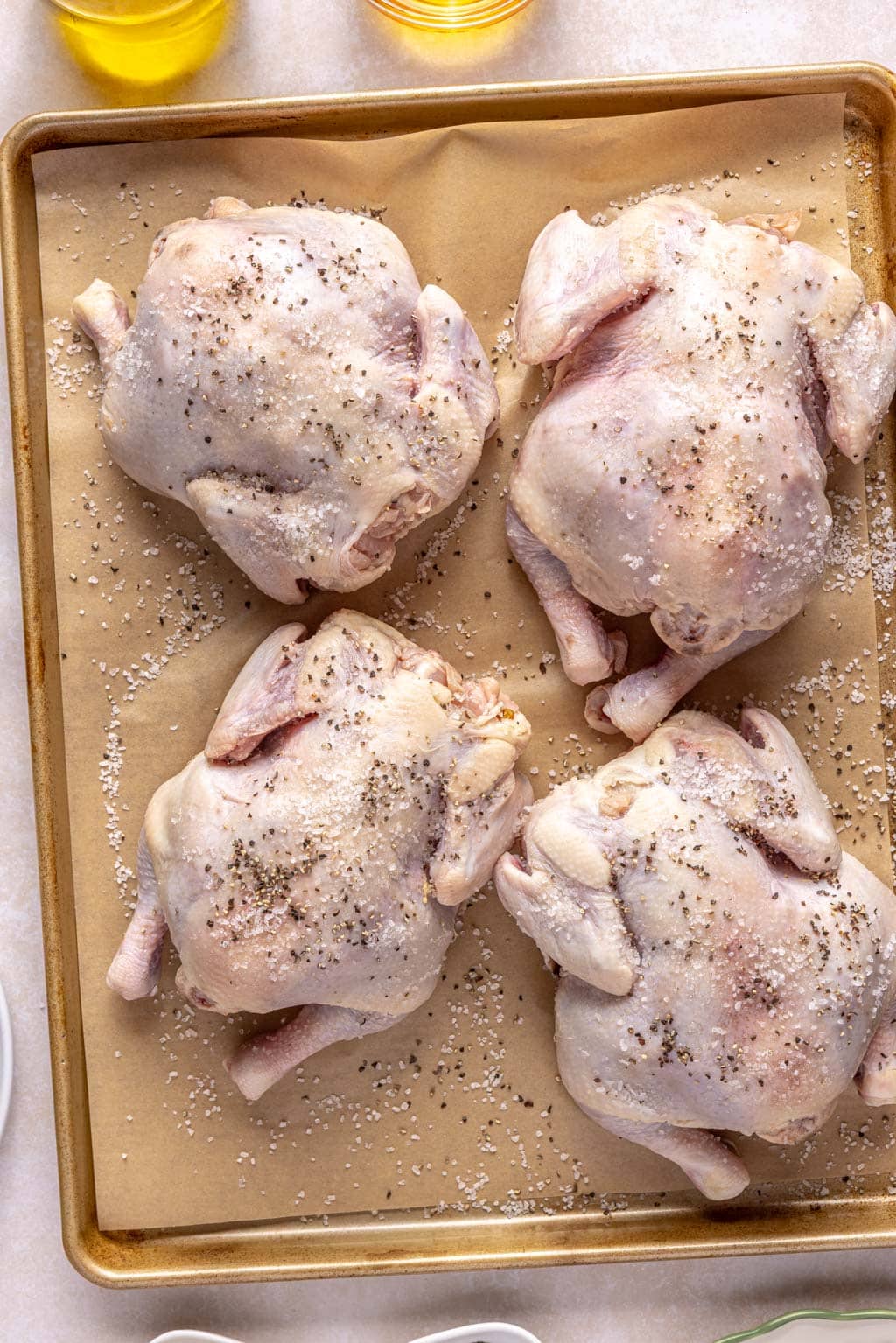 Four seasoned Cornish hens on a baking tray. 