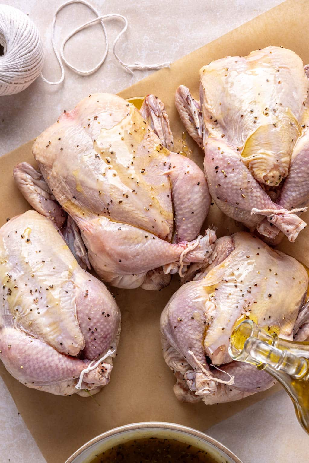 Four trussed Cornish hens being drizzled with oil. 