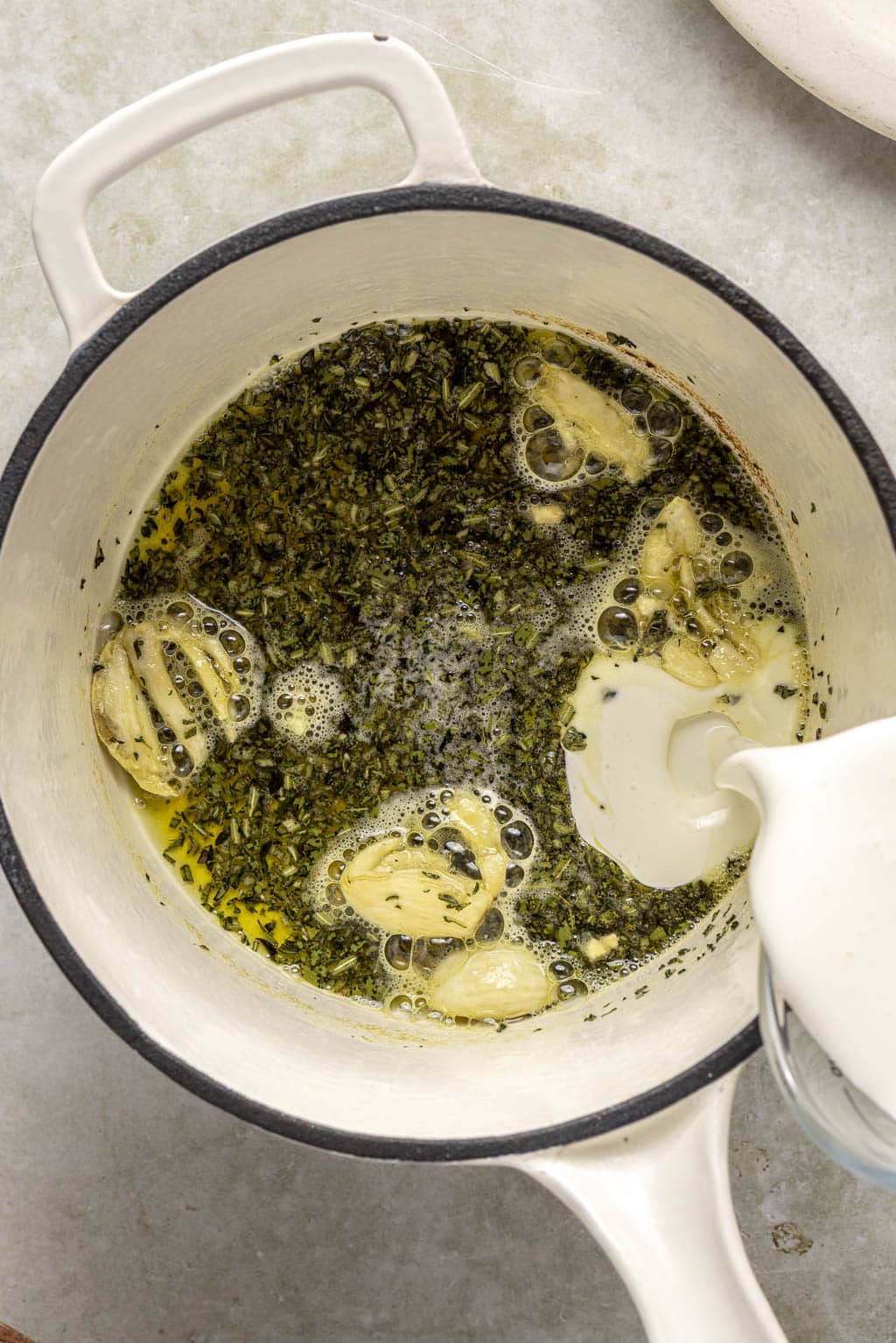 Heavy cream being poured into a saucepan of garlic butter. 