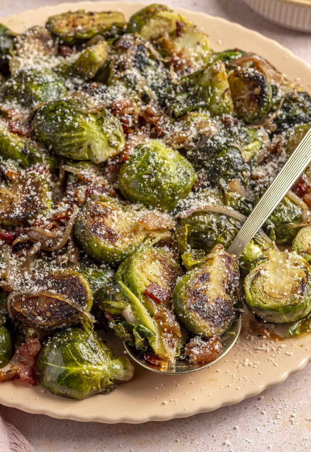 Crispy miso Brussels sprouts on a platter topped with bacon and grated Parmesan. 