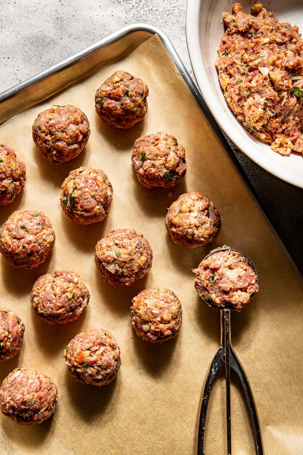 Mixed meatballs being scooped onto a baking sheet