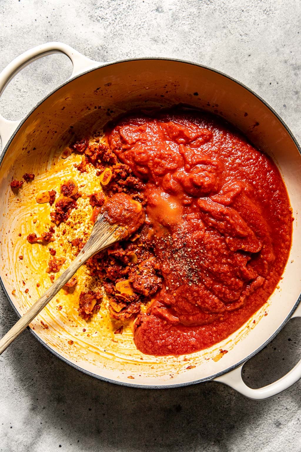 Tomato paste and crushed tomatoes being added to the sauce