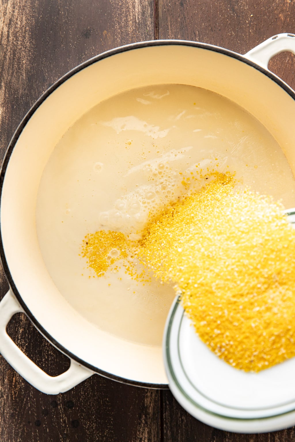 polenta being added to the milk and chicken stock in a dutch oven